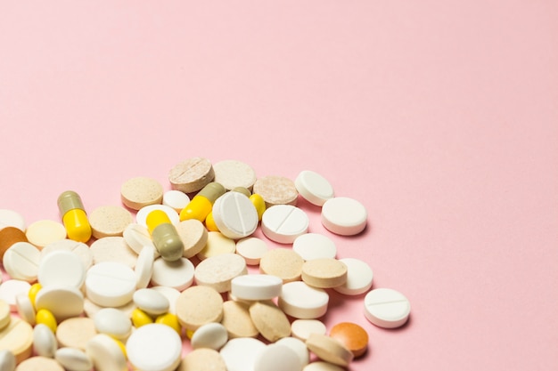 Pastillas de diferentes tamaños y colores sobre un fondo rosa claro. Concepto de industria farmacéutica, vitaminas y minerales diarios para mujeres. Embarazo, menopausia