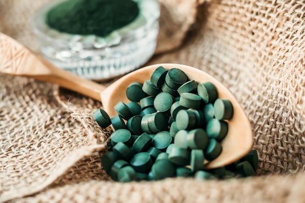 Pastillas de espirulina de algas, chlorella en una cuchara de madera de cerca. Súper alimento vegetariano con proteína vegetal