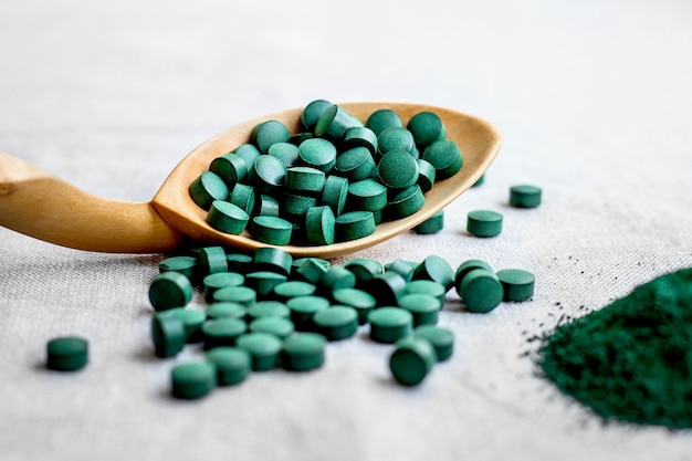 Pastillas de espirulina de algas, chlorella en una cuchara de madera de cerca. súper comida vegetariana con proteína vegetal sobre fondo claro