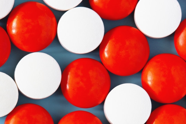 Pastillas de medicamentos blancos y rojos sobre superficie azul
