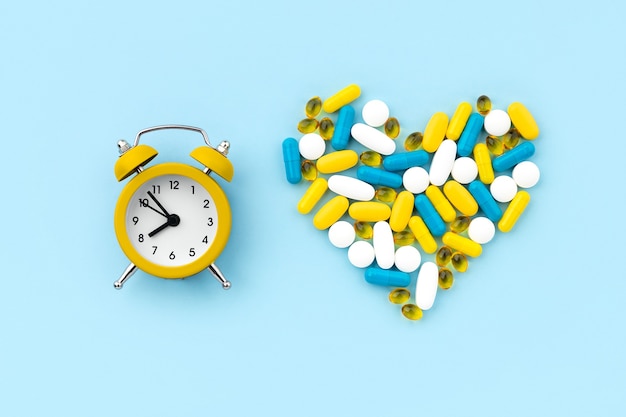 Pastillas médicas en forma de corazón con reloj despertador en azul