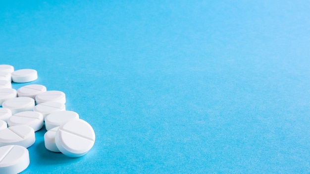 Pastillas médicas redondas blancas sobre un fondo azul. Pastillas blancas esparcidas sobre la mesa. El concepto de medicina, farmacia y salud. Copie el espacio Espacio vacío para texto o logotipo.