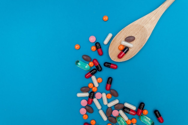 Pastillas multicolores en una cuchara de madera sobre un fondo azul.