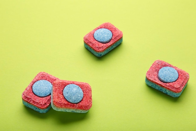 Pastillas rojas y azules para lavavajillas Detergentes para la higiene del hogar Cápsulas para lavavajillas sobre fondo verde