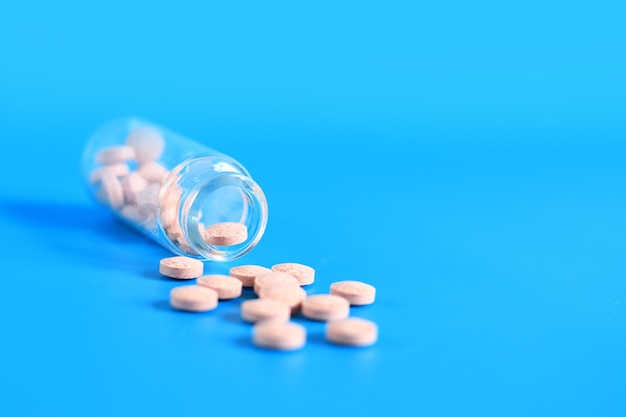 Las pastillas rosadas se derraman de una botella de vidrio sobre un fondo azul Vitamina B complejo espacio de copia