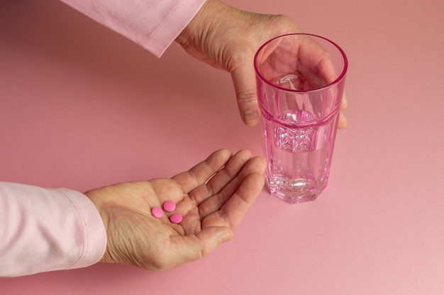 Pastillas y un vaso de agua en la mano de una anciana. Salud. Medicamento.