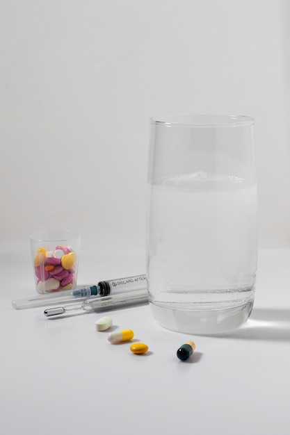 Pastillas en un vaso de plástico, un vaso de agua y una jeringa.