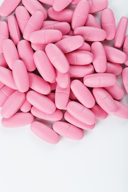 Pastillas de vitamina rosa para mujeres sobre un fondo blanco.
