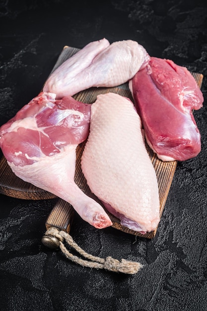 Patas de filete de pechuga de pato alas carne cruda en una tabla de cortar de carnicero Fondo negro Vista superior