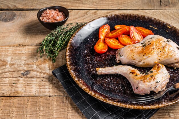 Patas de liebre al horno en un plato con tomate. Fondo de madera. Vista superior. Copie el espacio.