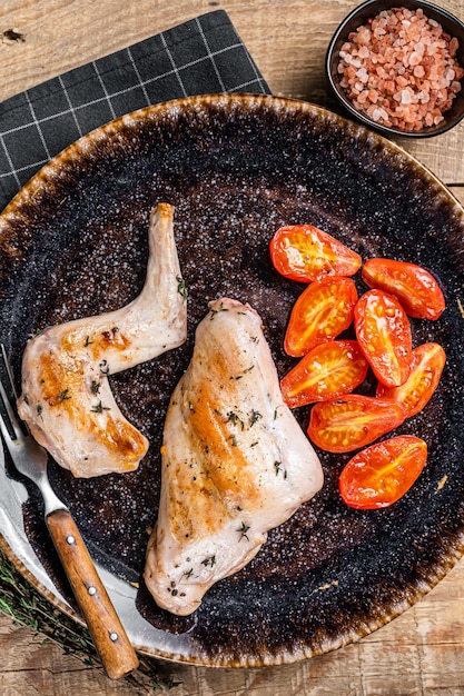 Patas de liebre al horno en un plato con tomate. Fondo de madera. Vista superior.