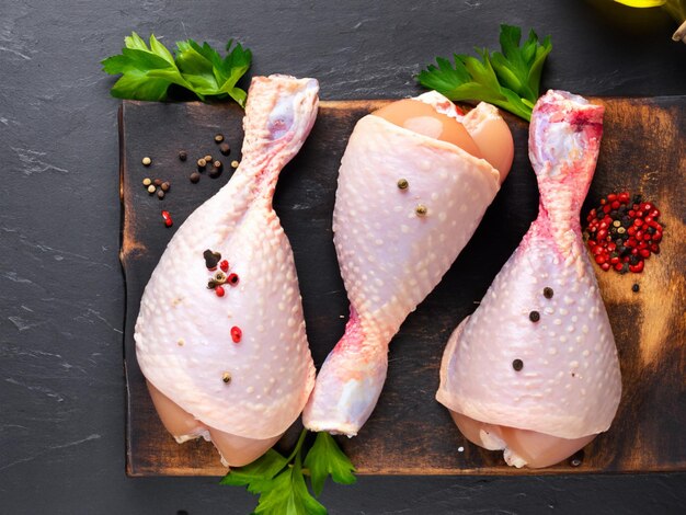 Patas de pollo crudas con especias en una tabla de cortar de madera sobre un fondo de pizarra negra o hormigón