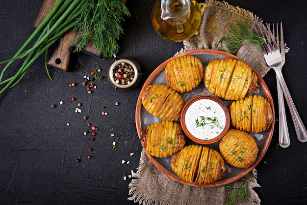 Patata al horno con hierbas y salsa en mesa negro.