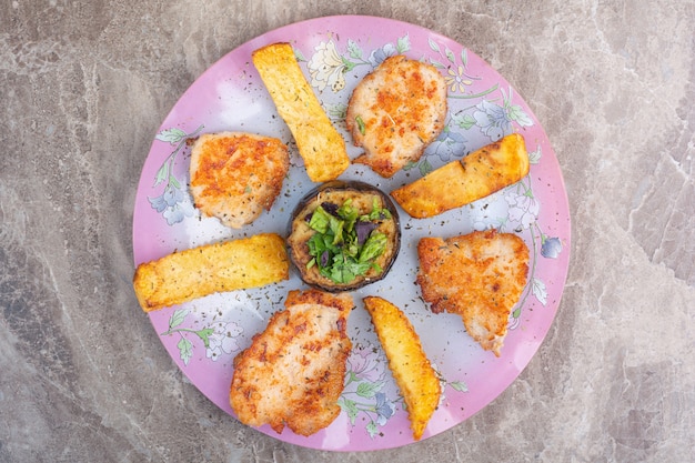 Patata, chuletas y berenjena en un plato, sobre el mármol.