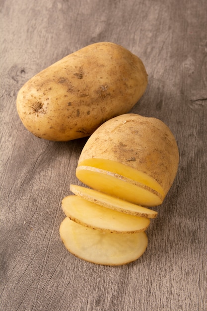 Foto patata cruda y patata cortada sobre fondo de madera