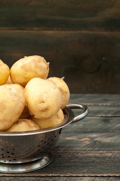 Foto patata joven orgánica en un recipiente sobre una mesa de madera.