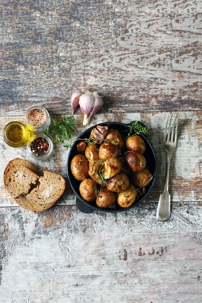 Patata rústica en una sartén. Papas pequeñas al horno en una cáscara con ajo y hierbas. Enfoque selectivo.