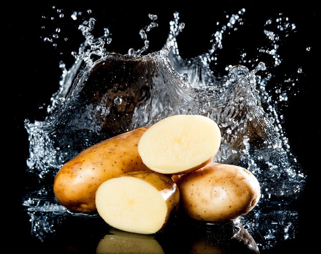 Foto patata con salpicaduras de agua sobre fondo negro