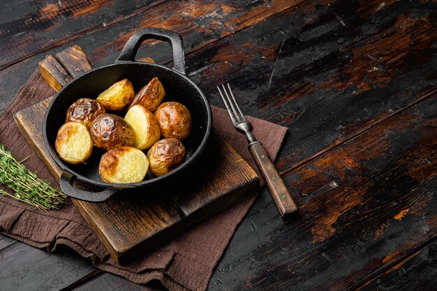 Patatas al ajo asadas, en una sartén de hierro fundido, sobre un fondo antiguo de madera oscura, con espacio para copiar texto