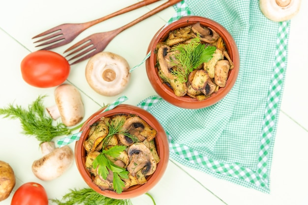 Patatas al horno con champiñones al horno en una olla de barro. Sobre un fondo verde claro. Vista superior.