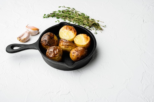 Patatas al horno con hierbas y ajo, en sartén de hierro fundido, sobre fondo de mesa de piedra blanca, con espacio para copiar texto