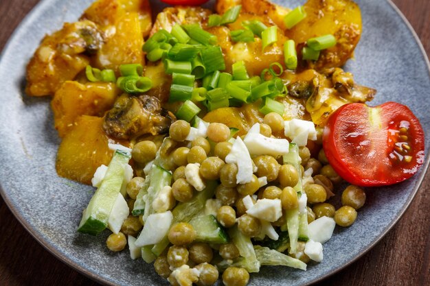 Foto patatas al horno con queso y costillas adornadas con tomates cherry y guisantes verdes en un plato cerrado