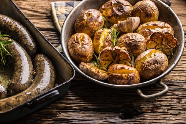 Patatas asadas con especias de ajo jitrnice jaternice y hierbas en sartén vintage.