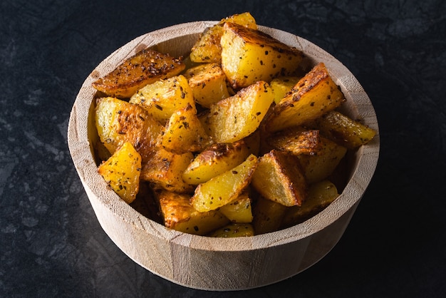 Patatas asadas en tazón de madera sobre superficie negra