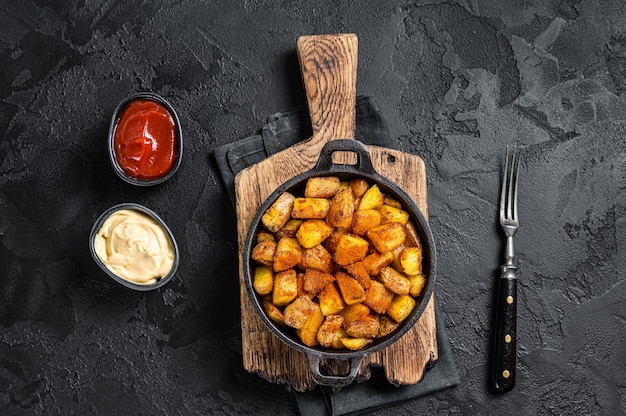 Patatas bravas, papas picantes, un plato español con papa frita y salsa picante de ajo. Fondo negro. Vista superior.