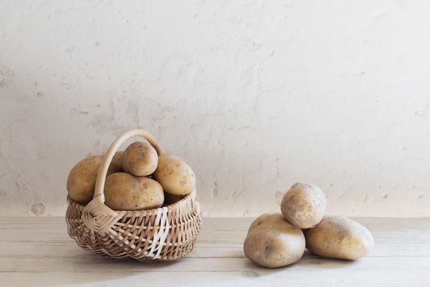 Patatas en la cesta en la pared vieja blanca