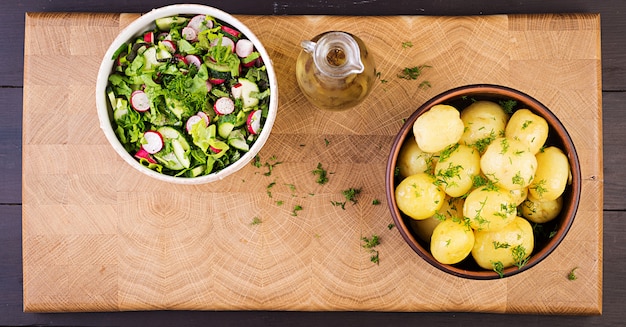 Patatas cocidas con eneldo en un tazón sobre tabla de madera. Vista superior