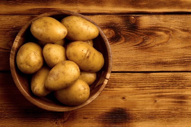 Patatas crudas nuevas en un plato de madera sobre fondo de madera