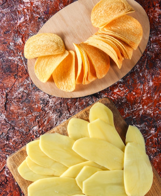 Patatas crudas en rodajas, chips fritos listos sobre fondo de hormigón rojo