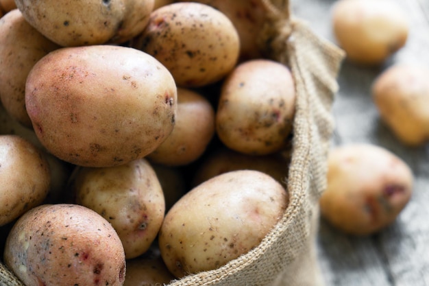 Patatas crudas en un saco de arpillera en las ásperas tablas de madera de cerca