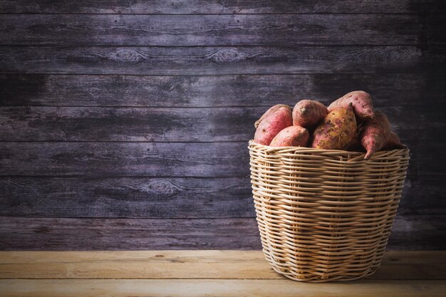 Patatas dulces rojas en la canasta exhibición de alimentos crudos en el fondo de la mesa de madera con espacio de copia