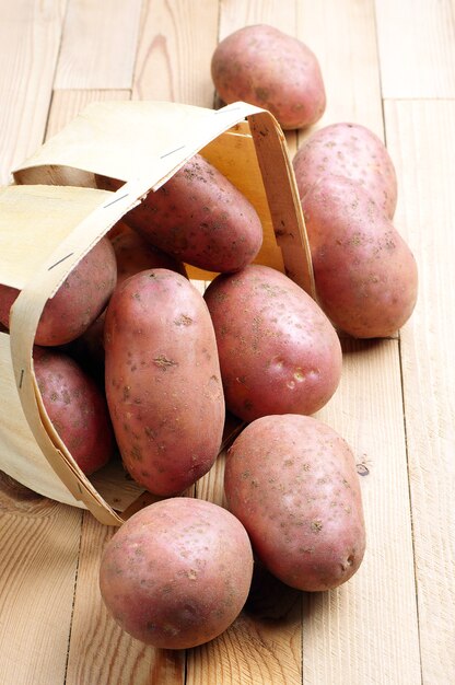 Patatas frescas en la canasta y cerca sobre fondo de madera