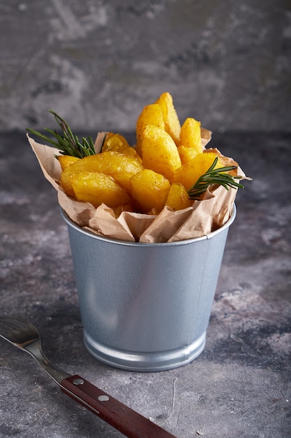 Foto patatas fritas al estilo country. papas a la barbacoa. en un recipiente metálico sobre un fondo gris.