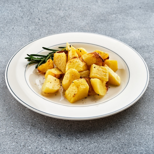 Patatas fritas al horno con romero en un plato blanco.