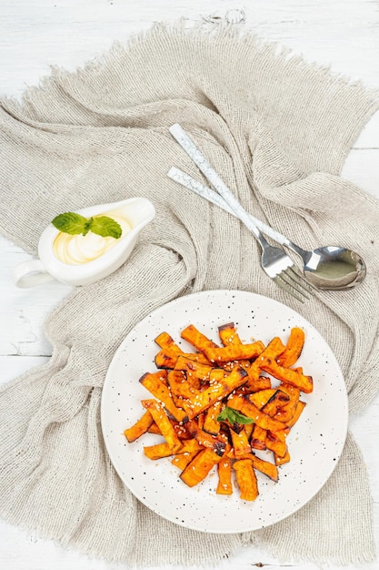 Patatas fritas de batata orgánicas al horno con especias y salsa Porción servida de vegetales dulces y cubiertos