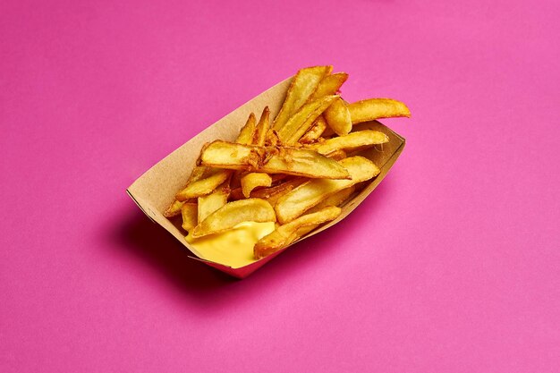 Patatas fritas en una caja de cartón sobre un fondo rosa.