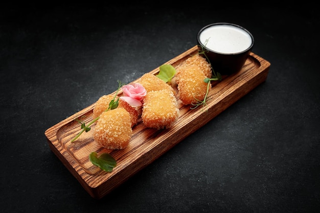 Patatas fritas Camembert con salsa sobre una tabla de madera sobre un fondo oscuro