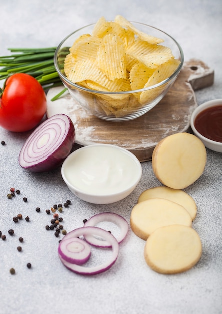 Patatas fritas caseras orgánicas frescas chips en recipiente de vidrio con crema agria y cebolla roja en la mesa de la cocina ligera