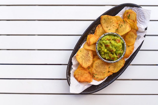 Patatas fritas caseras con salsa vegetariana de aguacate y verduras sobre mesa de madera blanca