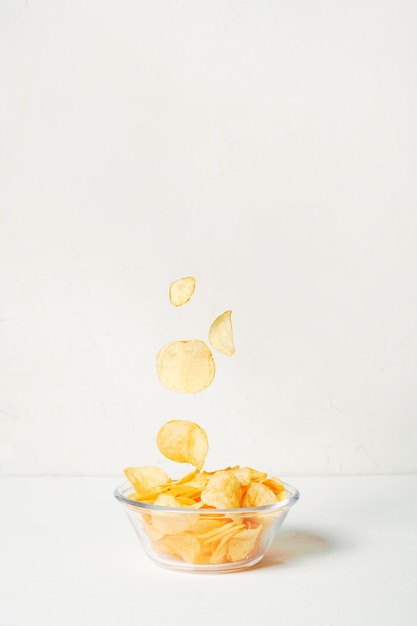 Patatas fritas cayendo en un recipiente de vidrio sobre fondo blanco.