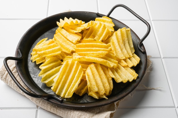 Patatas fritas corrugadas doradas sobre fondo de mesa de baldosas cuadradas de cerámica blanca