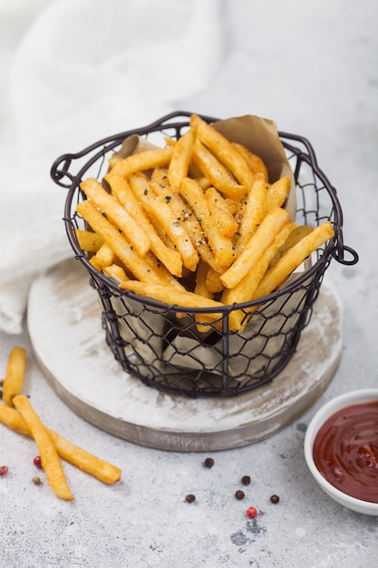 Patatas fritas en un cubo de aperitivos con salsa de tomate y pimienta sobre fondo de mesa de luz Macro