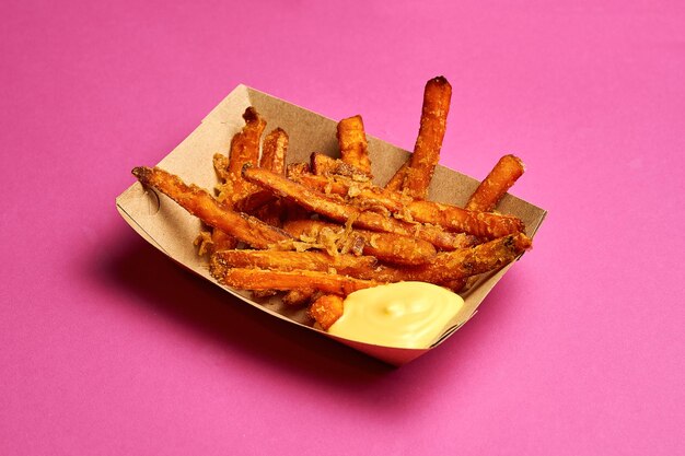 Patatas fritas dulces en una caja de cartón sobre un fondo rosa.