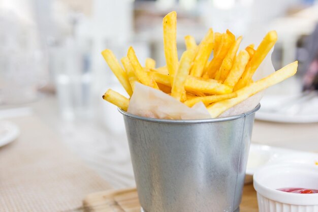 Patatas fritas envueltas con papel en un pequeño cubo inoxidable en una mesa de madera enfoque selectivo