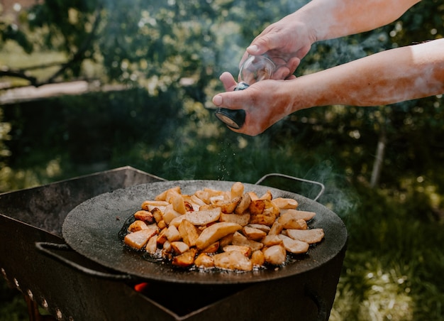 Patatas fritas jugosas con costra cocinadas en una sartén negra grande a la parrilla. fondo borroso