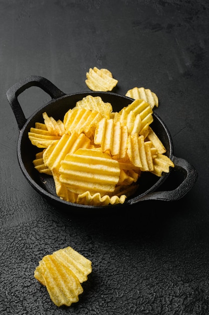 Patatas fritas ligeramente saladas onduladas sobre fondo de mesa de piedra oscura negra